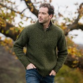 Man wearing a green sweater standing outdoors with trees in the background